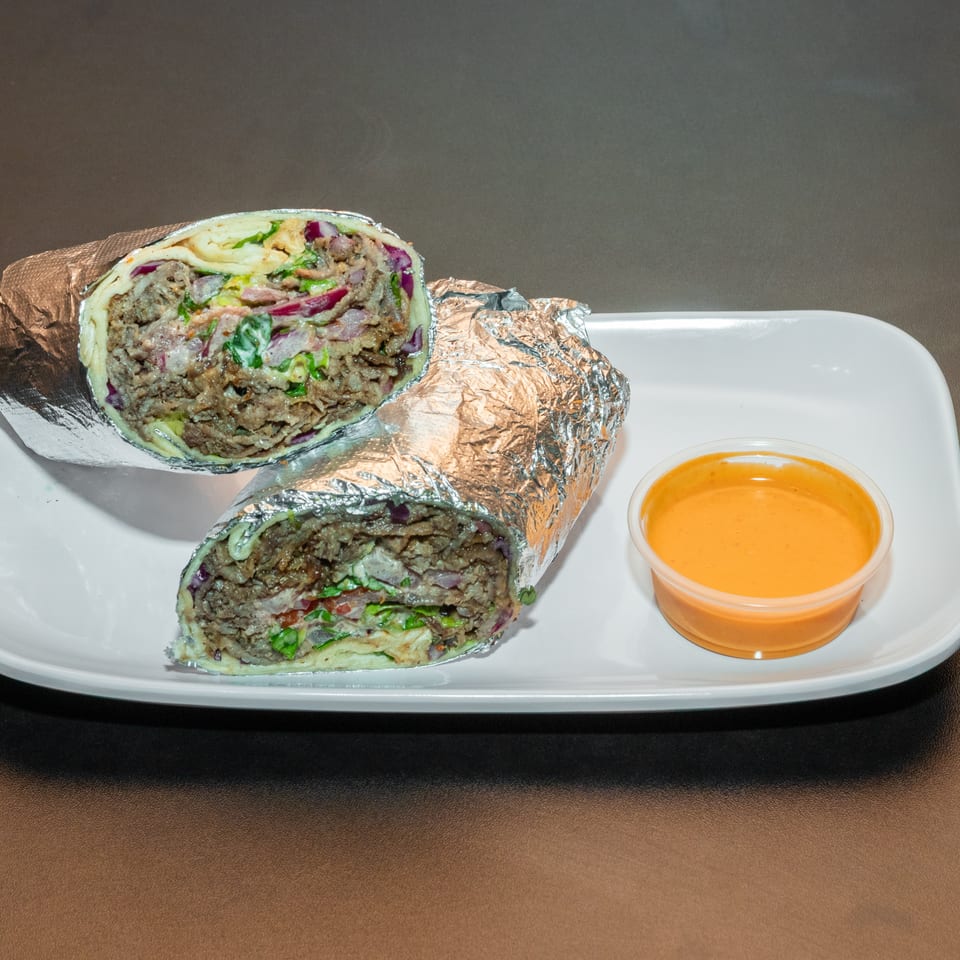 Two foil-wrapped meat and vegetable wraps cut in half on a white plate with orange dipping sauce.