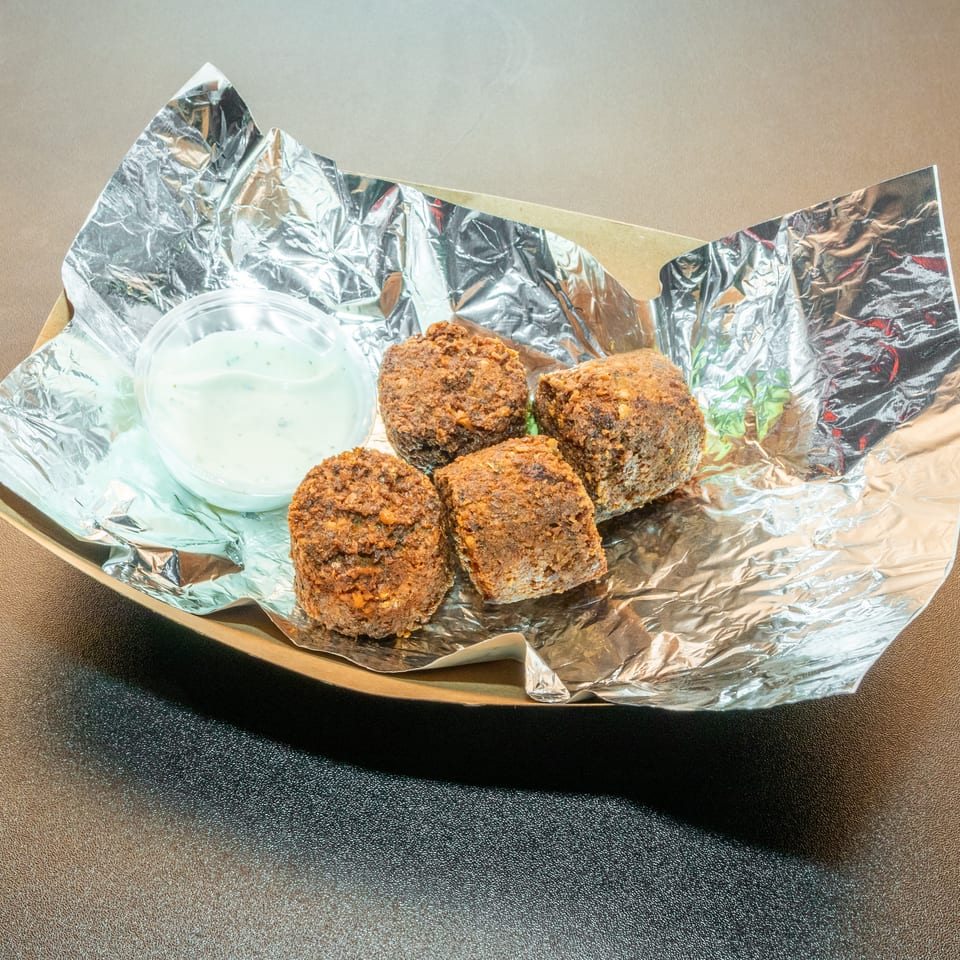 Four crispy fried patties served with creamy herb dipping sauce on foil-lined paper.