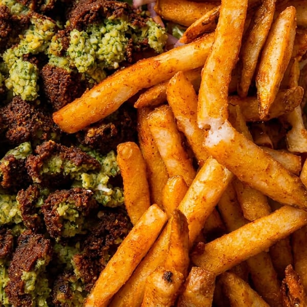 White rectangular plate filled with golden seasoned fries and crispy green-coated fried cauliflower bites on a wooden table.