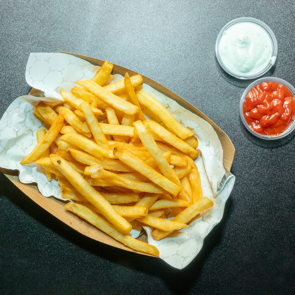 Crispy golden fries in a paper-lined tray with cups of ketchup and creamy herb dipping sauce.