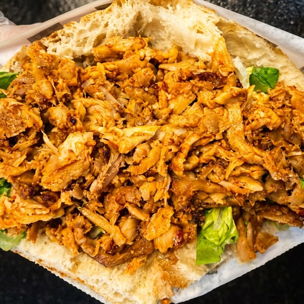 Close-up of a toasted flatbread sandwich filled with spiced shredded meat, crispy toppings, and green lettuce.