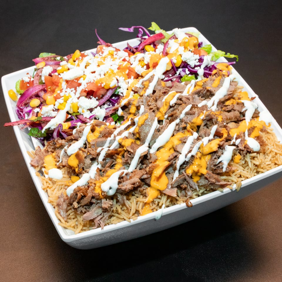 Square platter of seasoned rice topped with sliced meat, salad vegetables, corn, feta, and orange and white sauces.