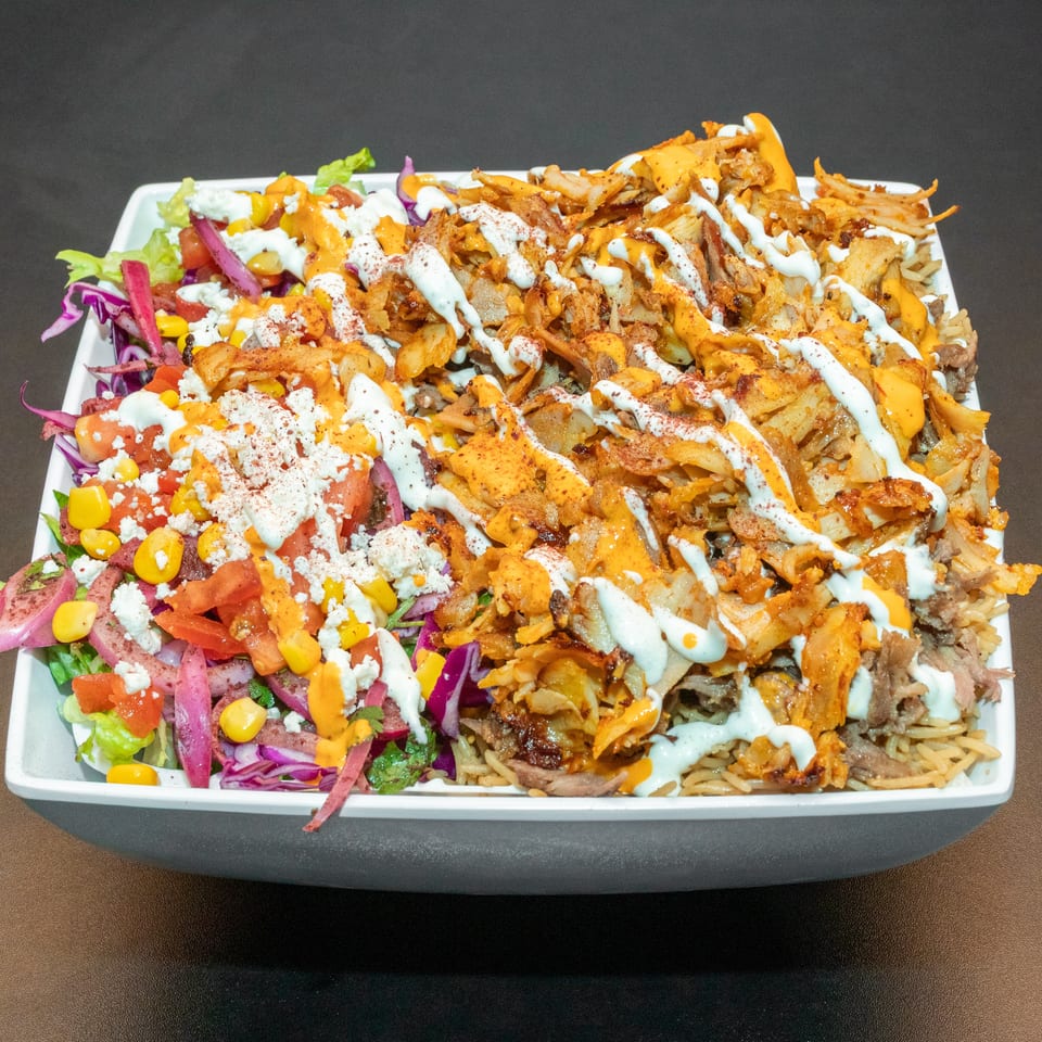 Loaded platter of shawarma, rice, salad, vegetables, feta, and creamy orange and white sauces.