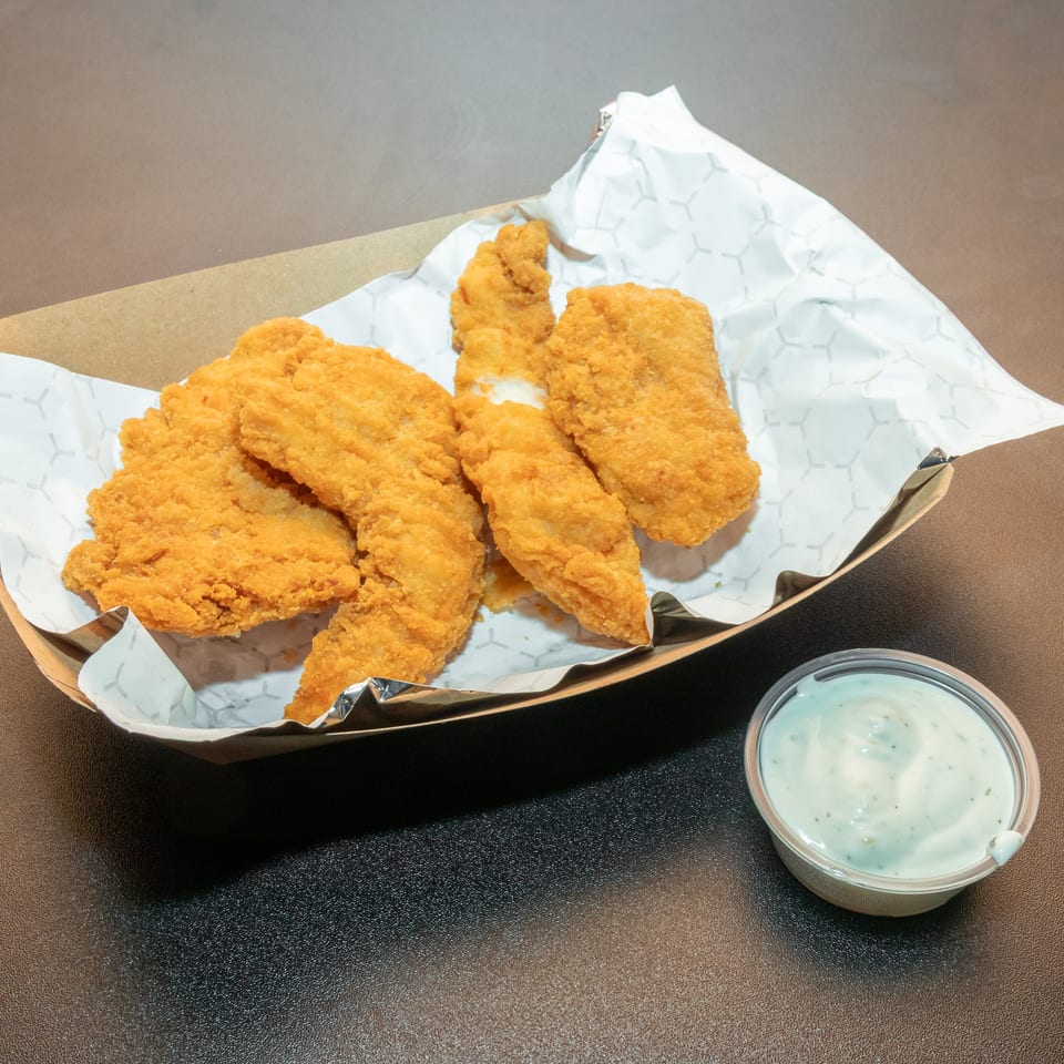 Crispy golden fried chicken strips served in a lined basket with a cup of creamy dipping sauce.